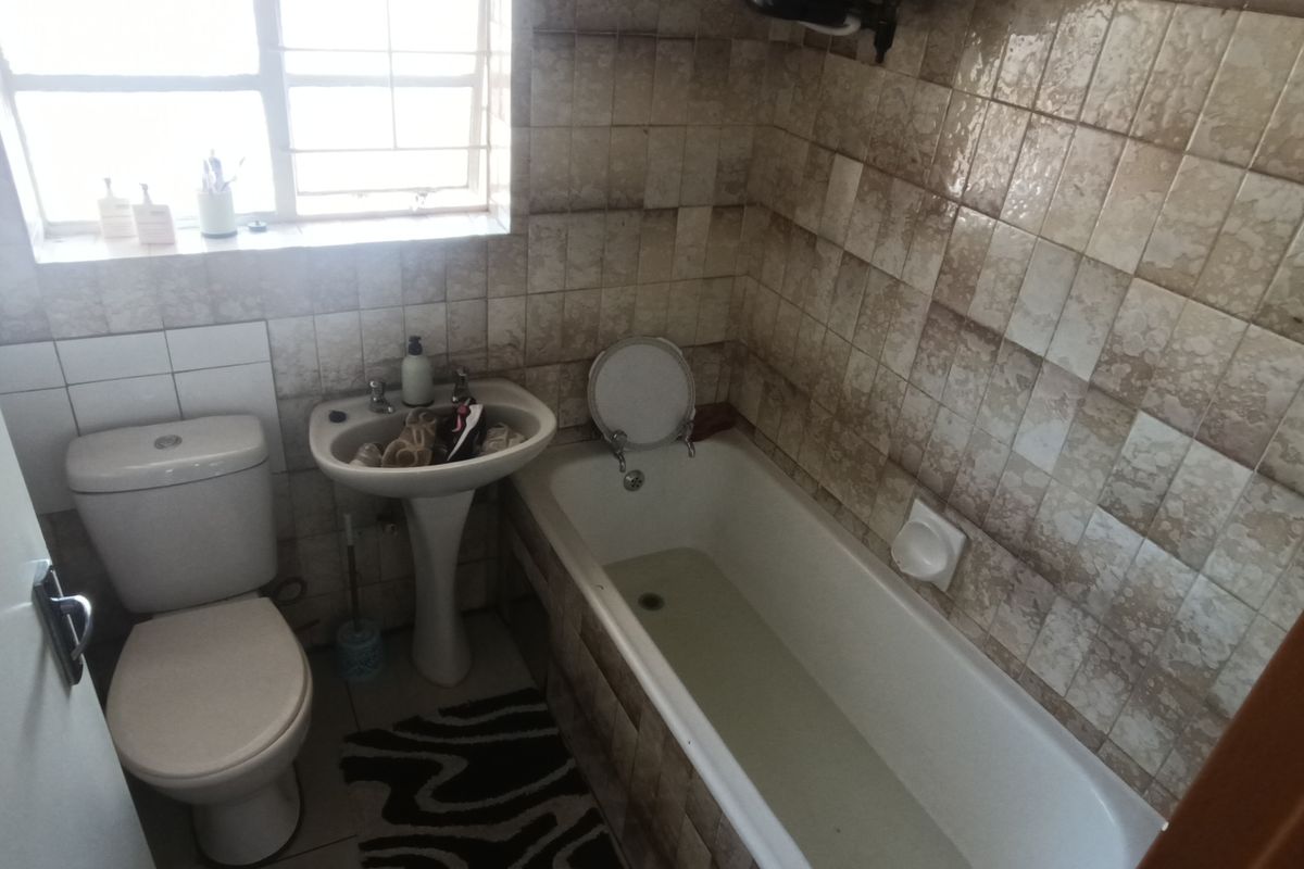 A compact bathroom featuring a standard bathtub, pedestal basin, and toilet with dated wall tiling throughout.