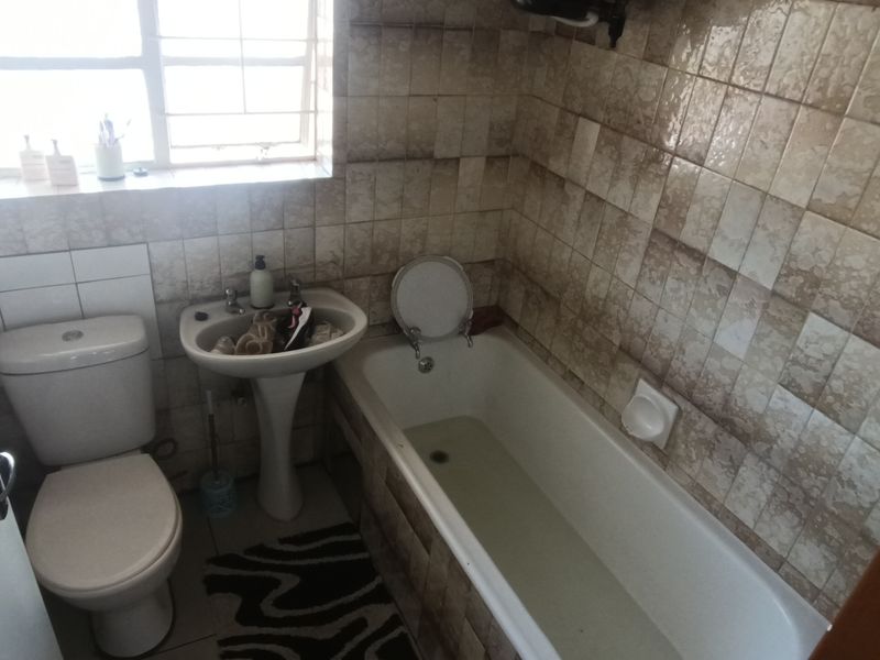 A compact bathroom featuring a standard bathtub, pedestal basin, and toilet with dated wall tiling throughout.