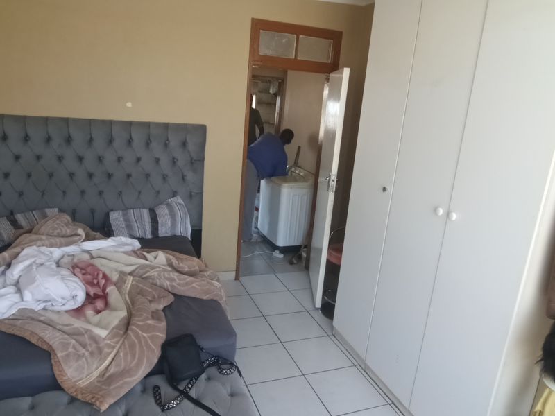 A bedroom featuring tiled flooring and a built-in wardrobe, with an adjacent utility area visible through the doorway.