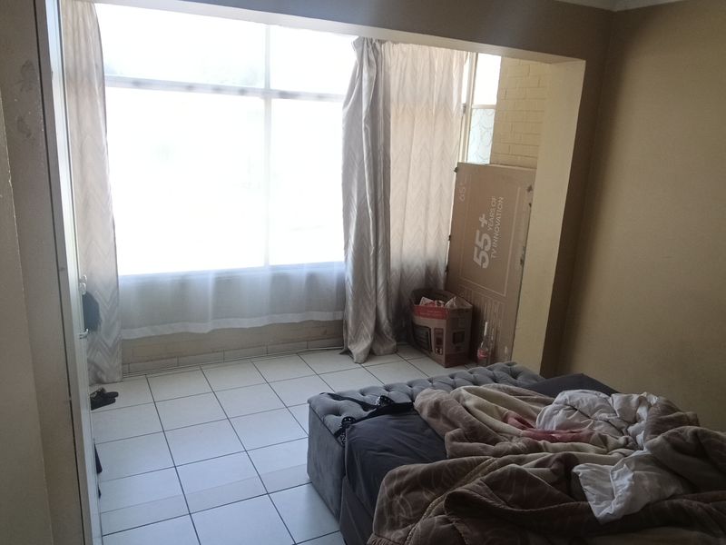 A bedroom featuring tiled flooring and a large window, with a recessed alcove area. The space requires cosmetic updates to improve its overall condition.