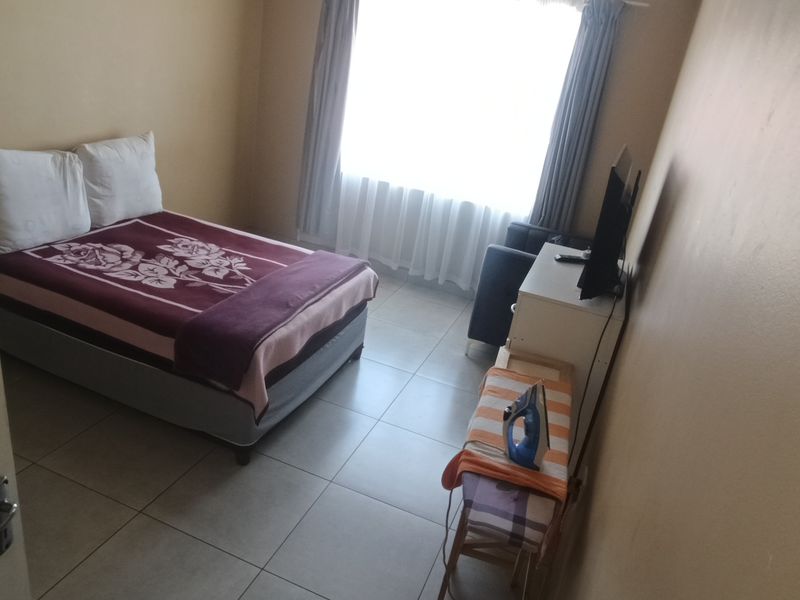 A functional bedroom featuring tiled flooring and a large window with curtain rails, providing natural light.