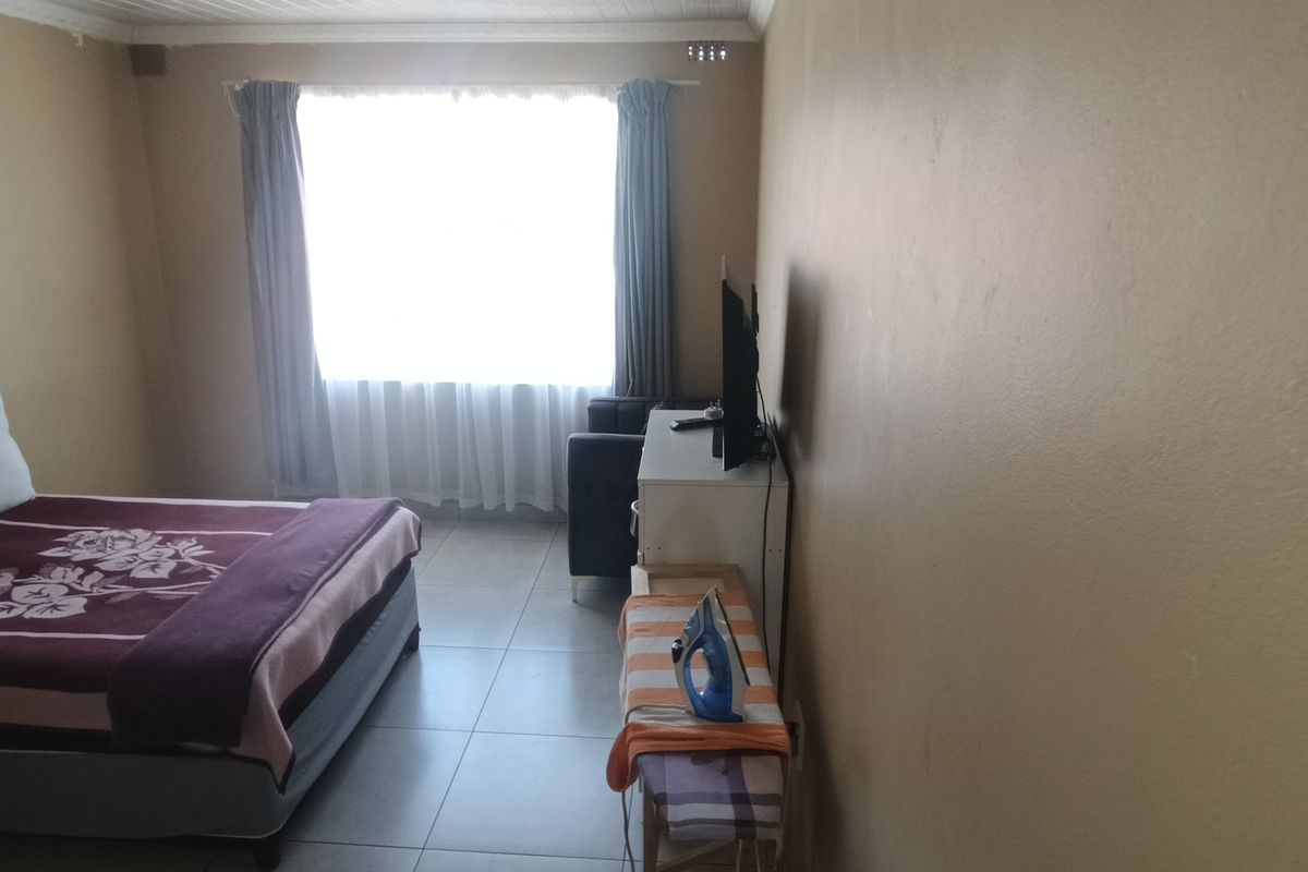 A simple bedroom featuring tiled flooring and a large window with curtain rails, providing natural light to the space.
