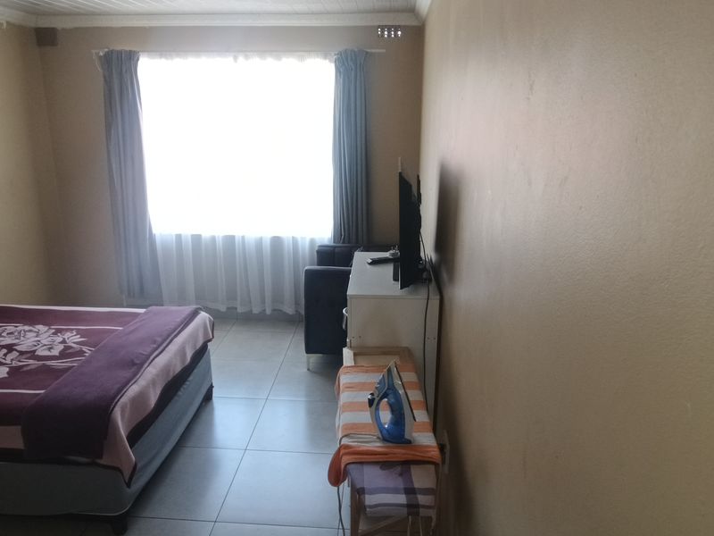 A simple bedroom featuring tiled flooring and a large window with curtain rails, providing natural light to the space.