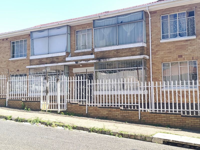 Front elevation of a multi-story brick apartment building featuring enclosed balconies, security fencing, and razor wire perimeter protection.