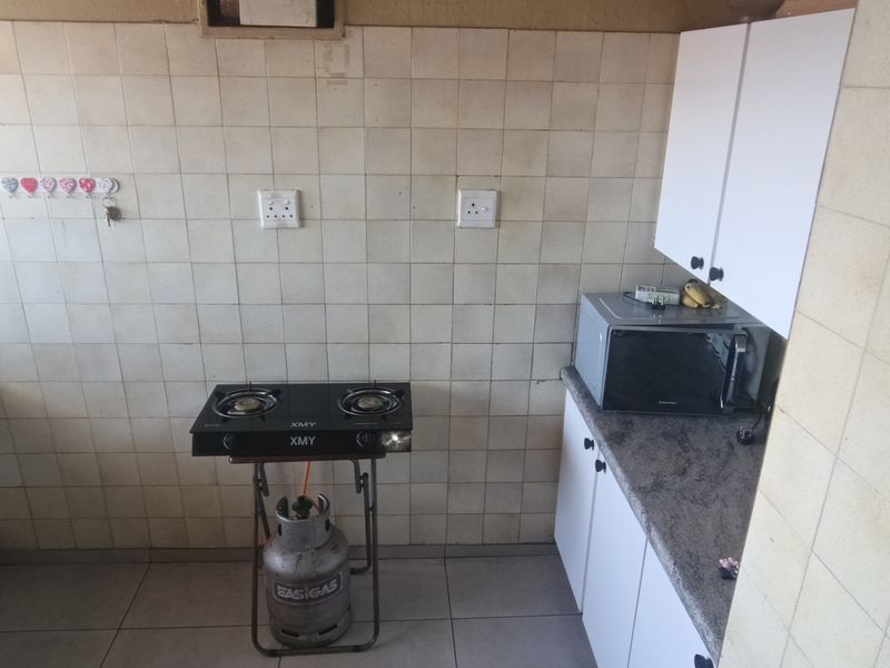 A functional kitchen area featuring tiled splashbacks, built-in cabinetry, and a double bowl sink, requiring cosmetic updates to improve the overall aesthetic.