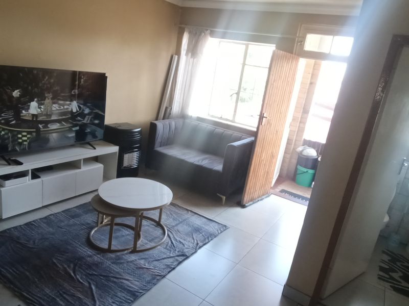 A living room area featuring tiled flooring, with an adjacent bathroom visible containing a pedestal basin and bathtub.
