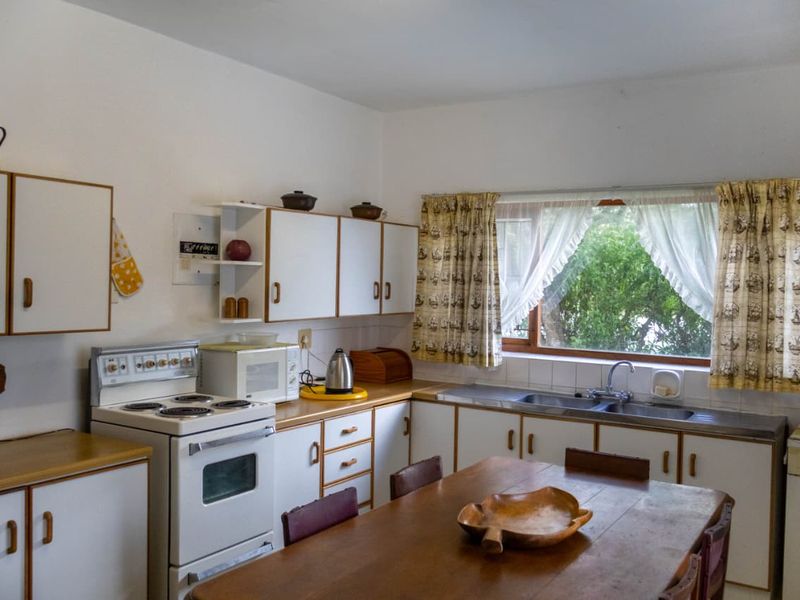 A dated kitchen featuring white cabinetry, laminate countertops, a freestanding stove, and a double sink with a window view.