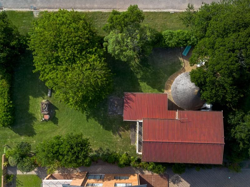 Aerial view of the property showcasing the main dwelling with a corrugated metal roof, a thatched section, and a spacious garden area.