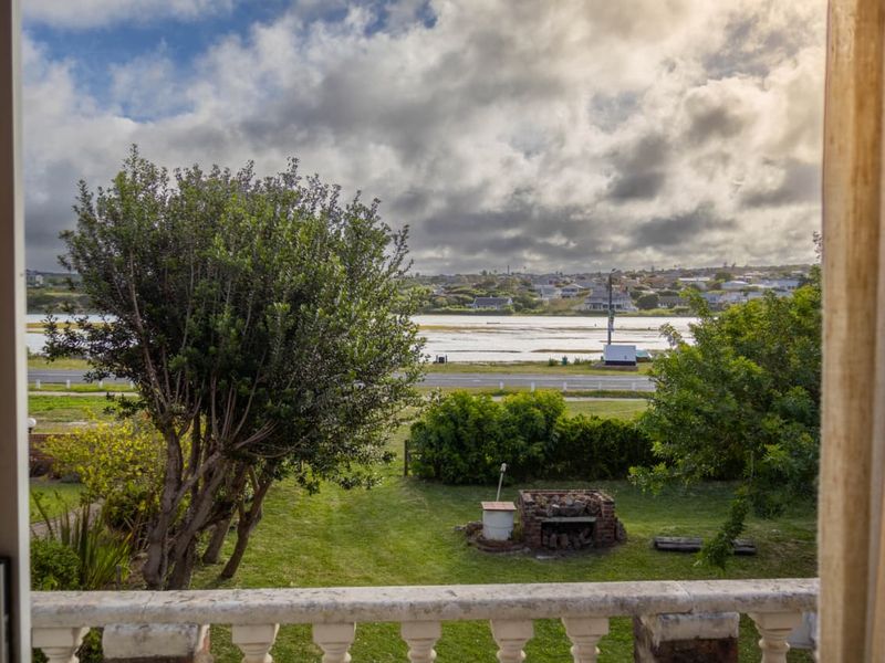 Scenic elevated view overlooking a garden, coastal road, and estuary, featuring a stone balustrade and a built-in brick braai area.