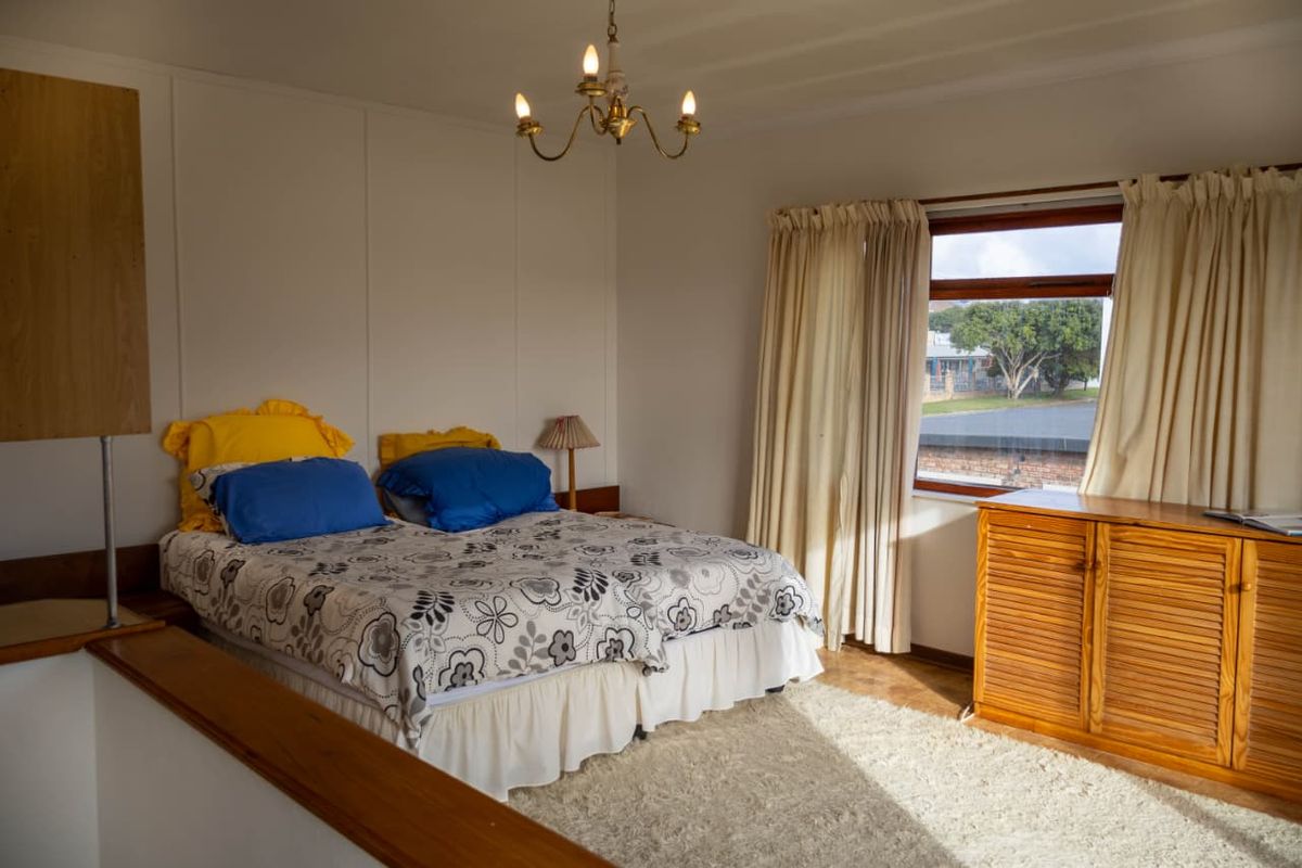 A bedroom featuring a built-in wooden cupboard, a classic chandelier, and a window with curtains.