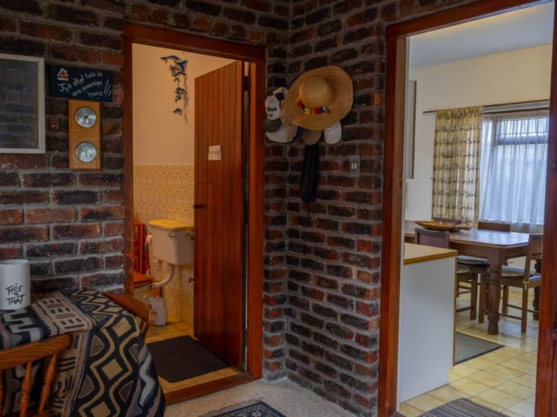 A hallway featuring exposed brick walls and wooden door frames, providing access to a bathroom and an adjacent dining area.
