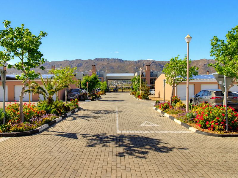 A well-maintained residential complex driveway featuring paved surfaces, landscaped garden beds, garage access, and solar panels on the building roofs.