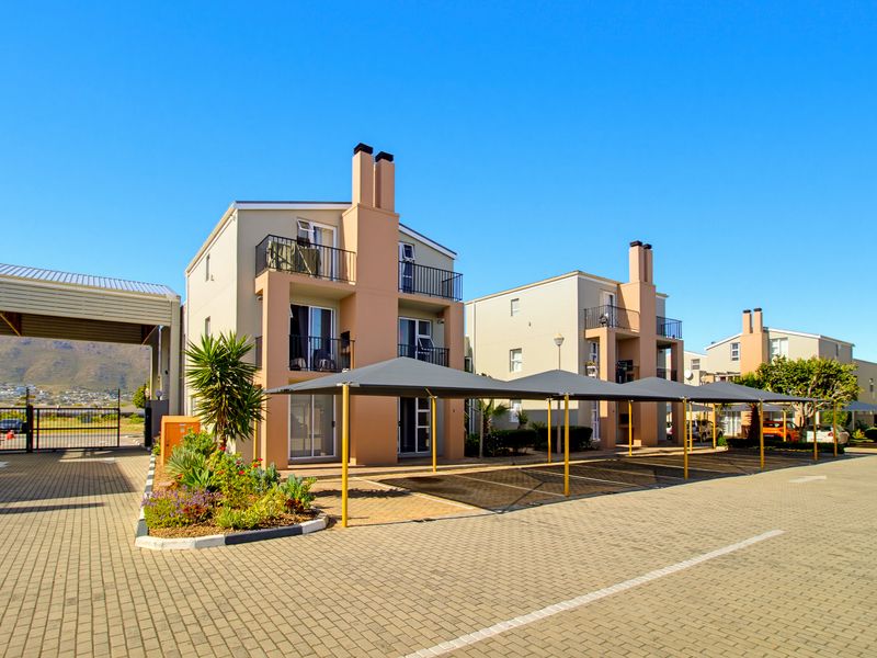 Exterior view of a modern apartment complex featuring paved parking areas with shade cloth carports, balconies, and well-maintained landscaping.