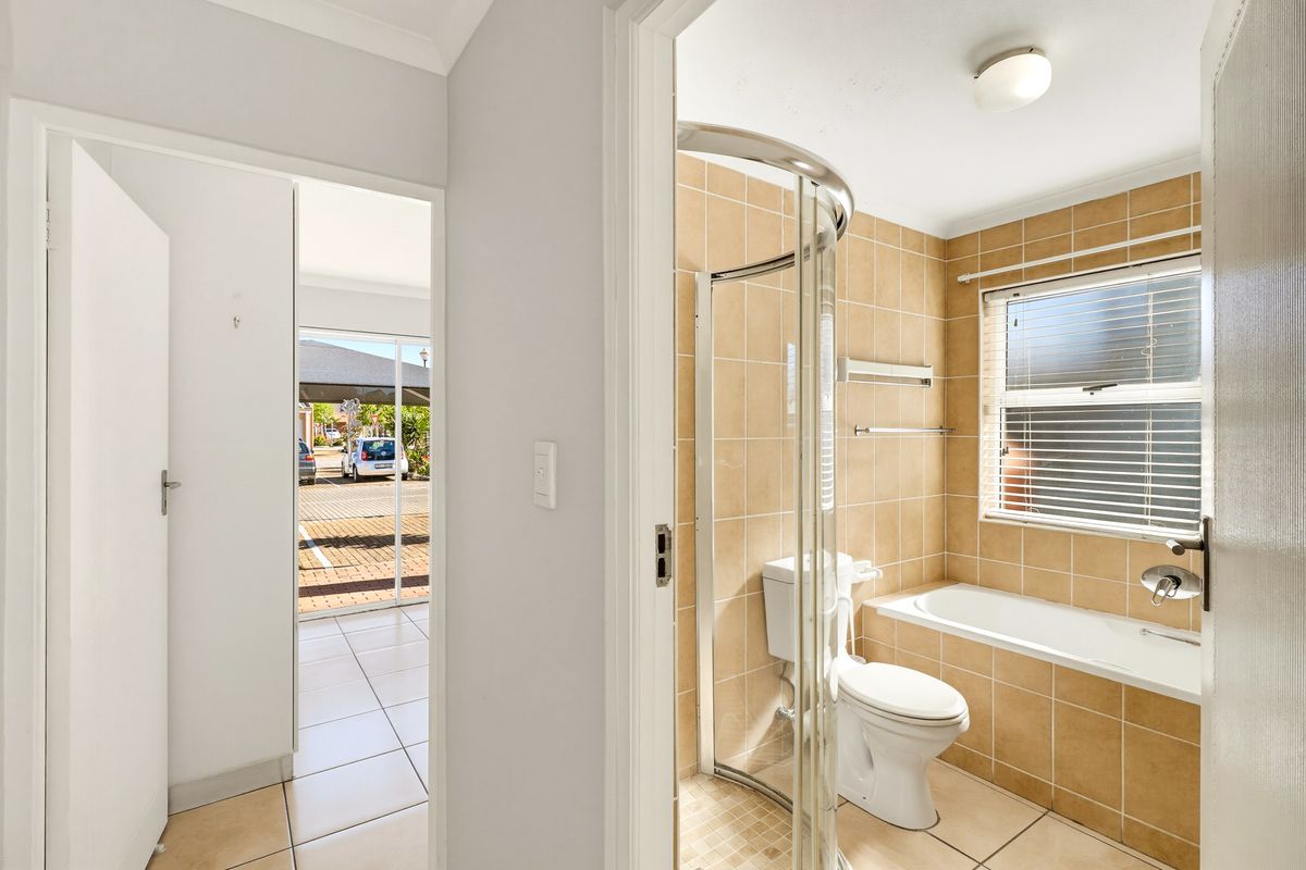 A functional bathroom featuring a curved glass shower enclosure, a built-in bathtub, and neutral ceramic wall and floor tiling.