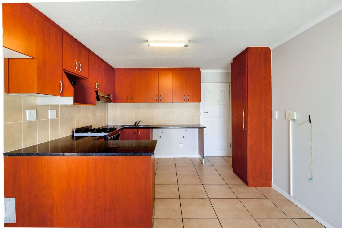 A functional kitchen featuring wood-finish cabinetry, granite countertops, a gas hob, and tiled flooring, offering a practical layout for culinary activities.