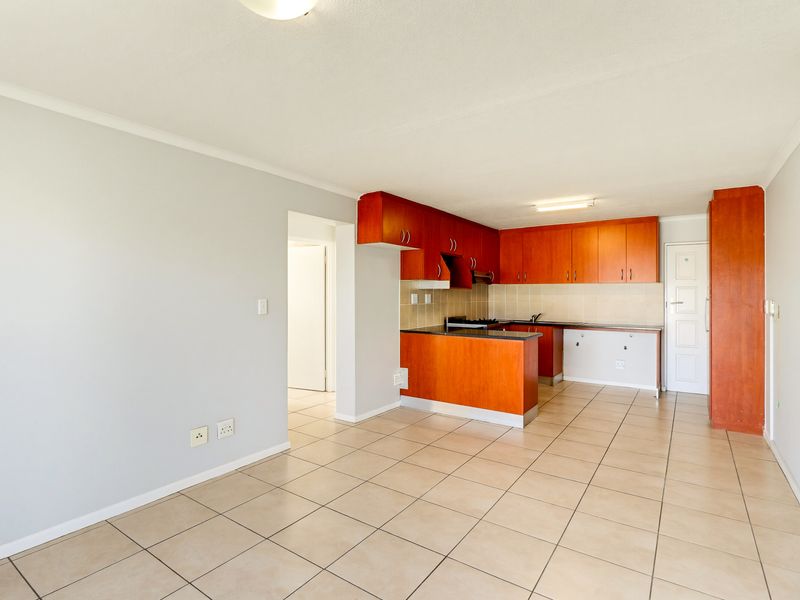 An open-plan living and kitchen area featuring tiled flooring, built-in wooden cabinetry, and a functional kitchen layout with a built-in hob and extractor.