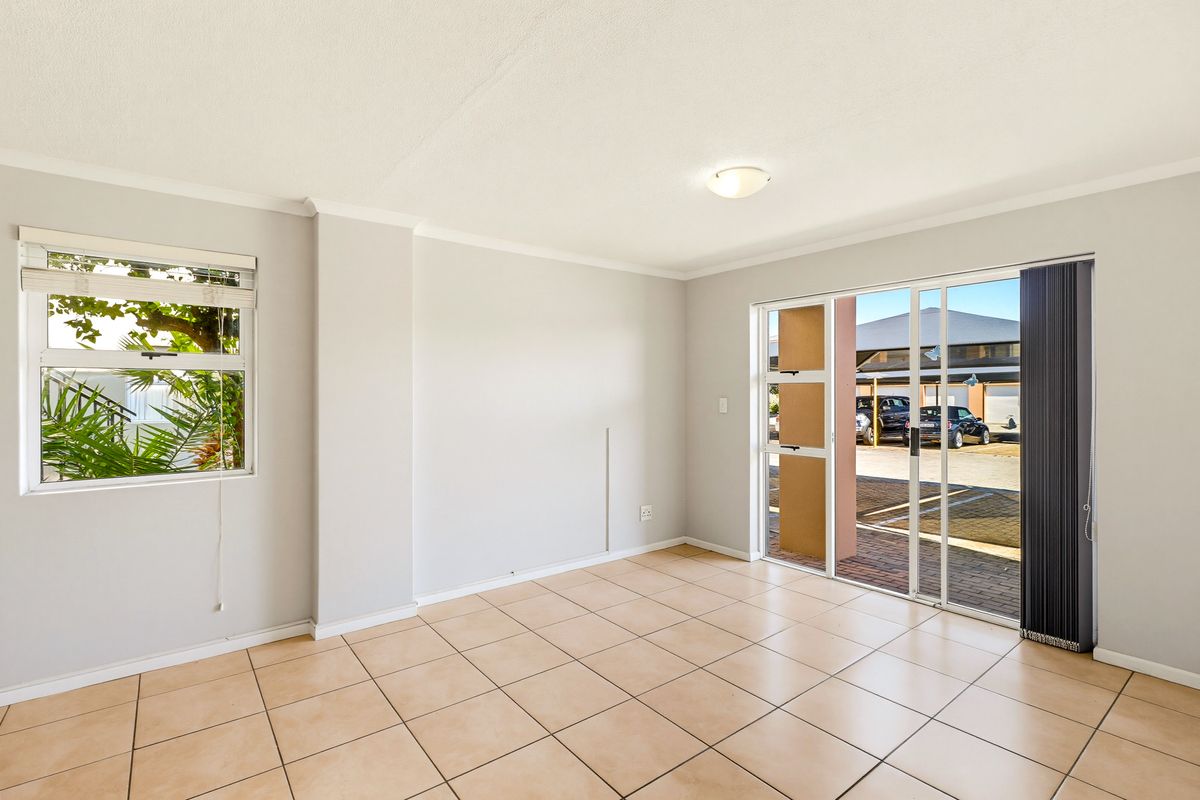 A bright, empty living room featuring neutral tiled flooring, a ceiling light, and a sliding glass door providing access to the exterior.