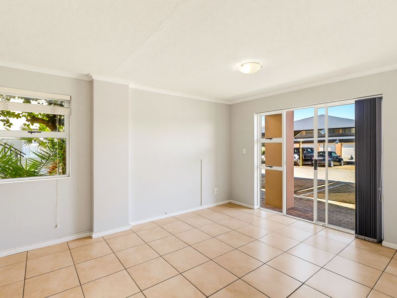 A bright, empty living room featuring neutral tiled flooring, a ceiling light, and a sliding glass door providing access to the exterior.