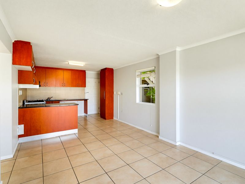 An open-plan living and kitchen area featuring tiled flooring, wooden cabinetry, and a functional layout, offering a blank canvas for personalization.