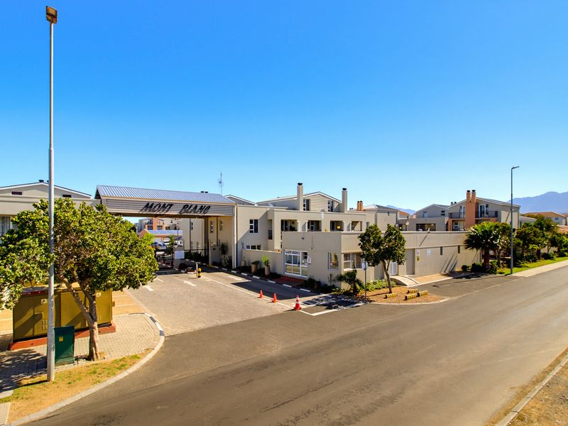 Exterior view of the Mont Blanc apartment complex entrance, featuring a gated access point, paved driveway, and well-maintained perimeter structures.