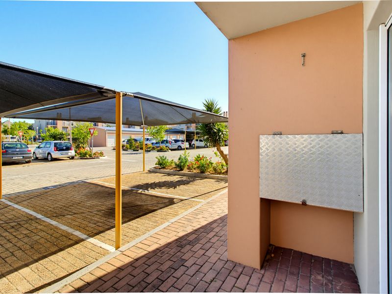 View of the apartment exterior featuring a paved driveway and a covered shade cloth carport parking area.
