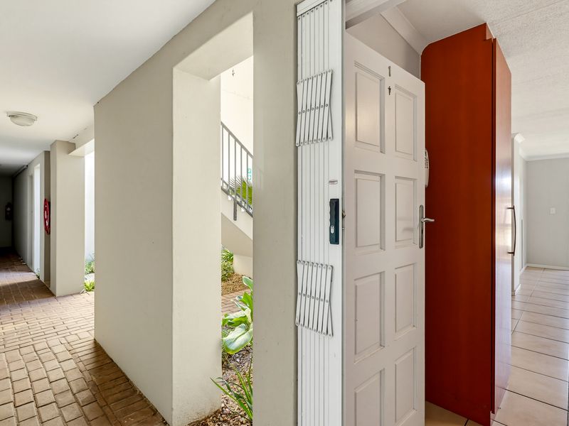 Entrance area featuring a security gate, tiled flooring, and a built-in cupboard, leading to an external brick-paved walkway.