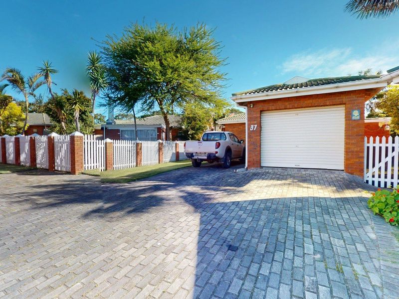 Front exterior view of a townhouse featuring a brick driveway, single garage with a roll-up door, and a white picket fence.