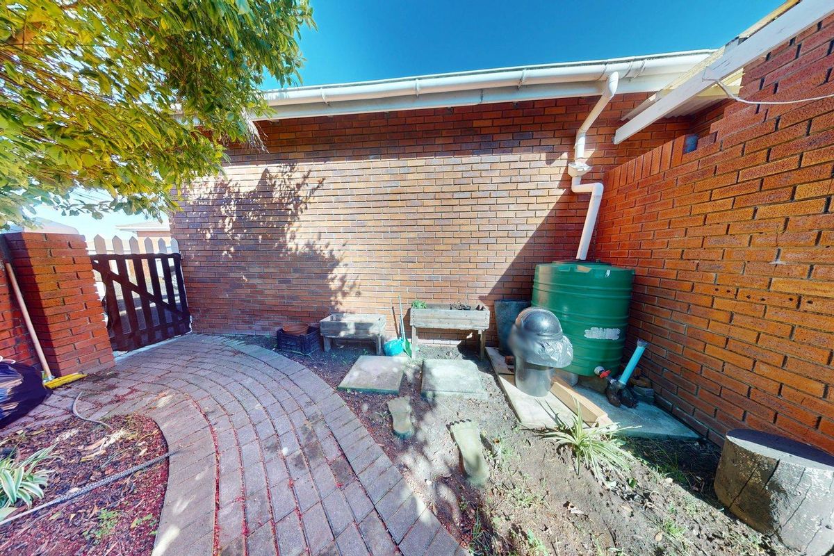 A rear exterior view of the townhouse featuring a brick facade, paved pathway, and a rainwater collection tank.
