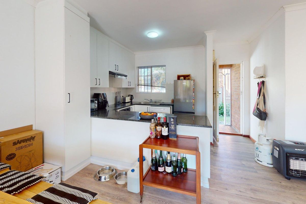 Compact kitchen featuring white cabinetry, granite countertops, and laminate flooring, with direct access to an exterior entrance.