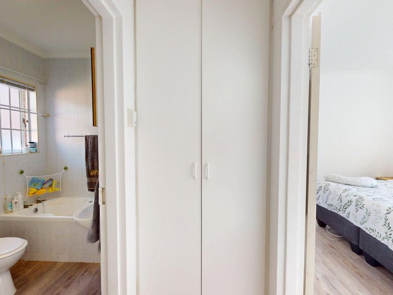 A hallway view showing access to a bathroom with a bathtub and toilet, alongside a bedroom with laminate flooring and built-in storage.