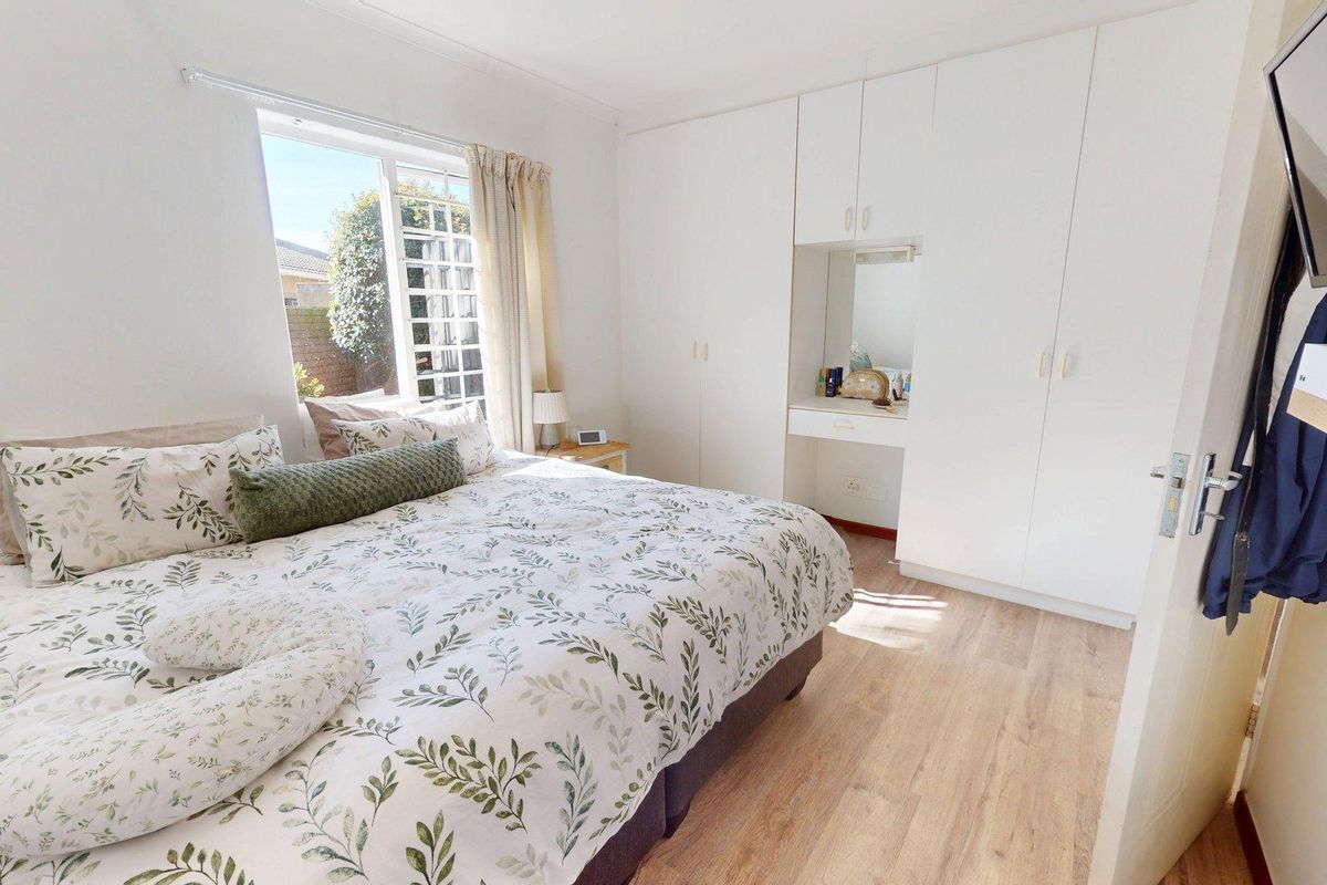 A bright bedroom featuring light-toned laminate flooring, ample built-in cupboard storage, and a dedicated vanity area with a mirror.