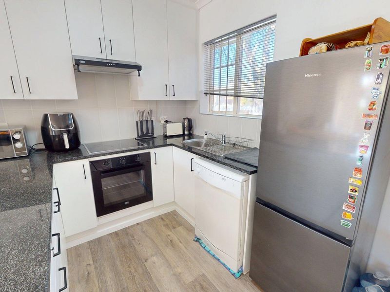 A functional kitchen featuring white cabinetry, granite countertops, integrated oven and hob, and durable laminate flooring.