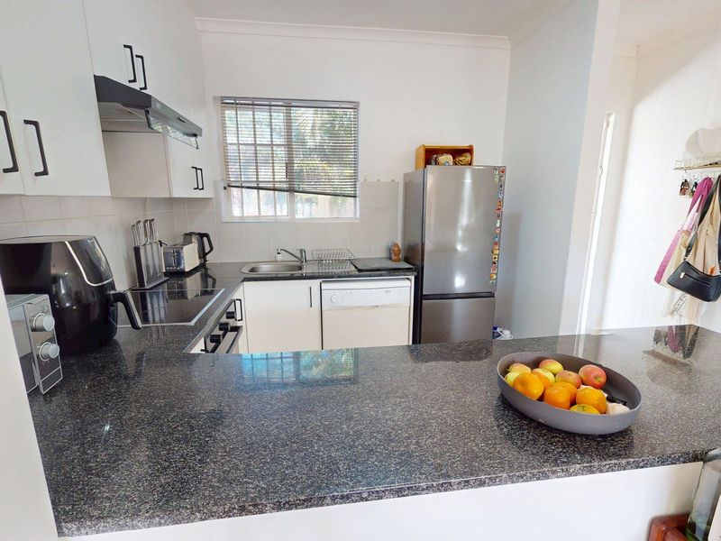 A functional kitchen featuring granite countertops, white cabinetry, a breakfast bar, and integrated appliances, providing a clean and practical workspace.