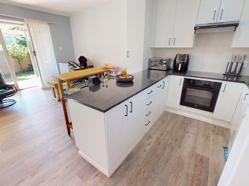 Open-plan kitchen featuring granite countertops, built-in oven, and hob, flowing into a living area with direct access to the rear garden via sliding doors.