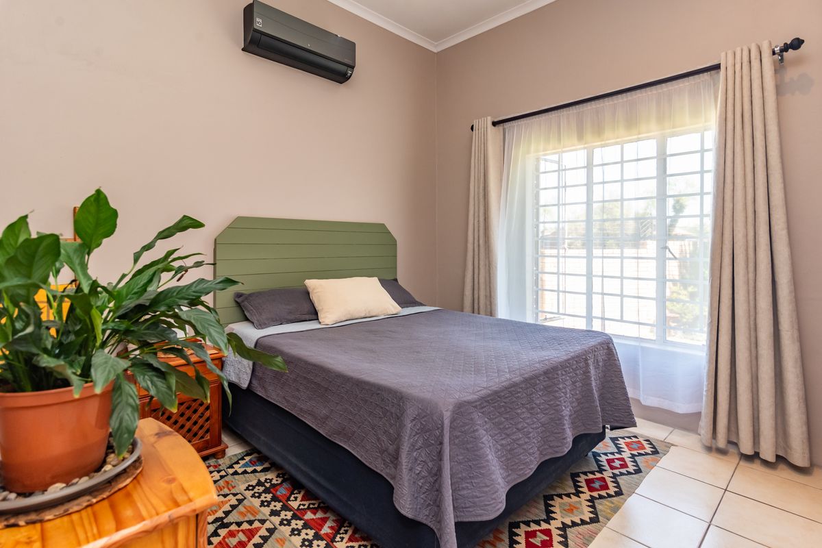 A well-maintained bedroom featuring tiled flooring, a wall-mounted air conditioning unit, and a window fitted with security bars.