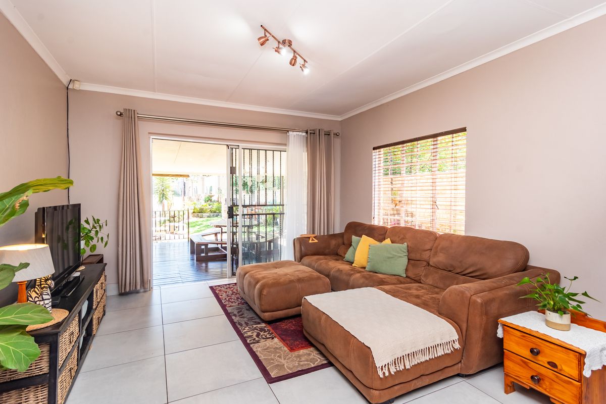 A bright living room featuring tiled flooring, track lighting, and a sliding glass door providing direct access to the outdoor patio area.