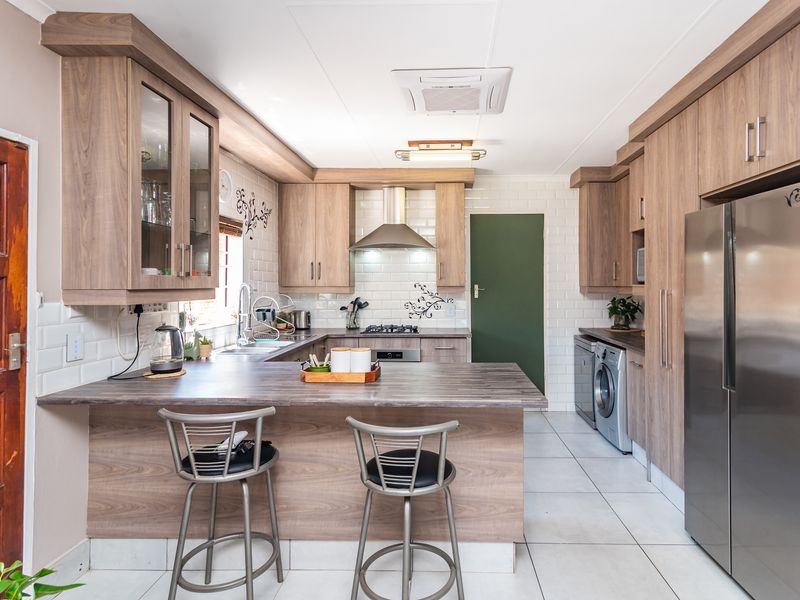 Modern kitchen featuring wood-look cabinetry, subway tile backsplash, integrated appliances, and a breakfast bar with ample counter space.