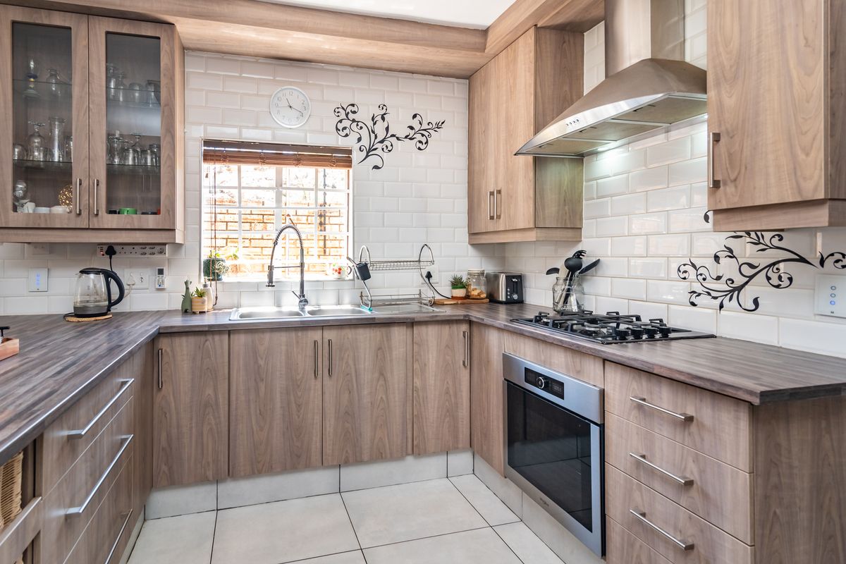 A well-maintained kitchen featuring wood-look cabinetry, subway tile backsplash, stainless steel appliances, and a gas hob with an integrated extractor fan.