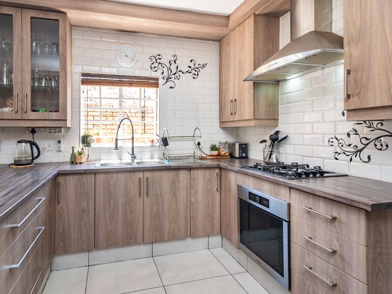 A well-maintained kitchen featuring wood-look cabinetry, subway tile backsplash, stainless steel appliances, and a gas hob with an integrated extractor fan.