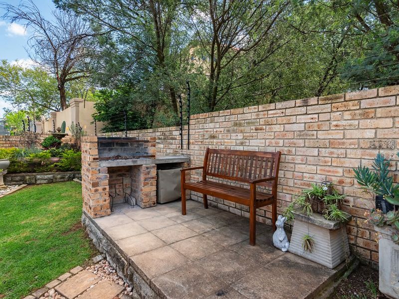 A private outdoor patio area featuring a built-in brick braai, paved flooring, and a secure brick boundary wall with electric fencing.
