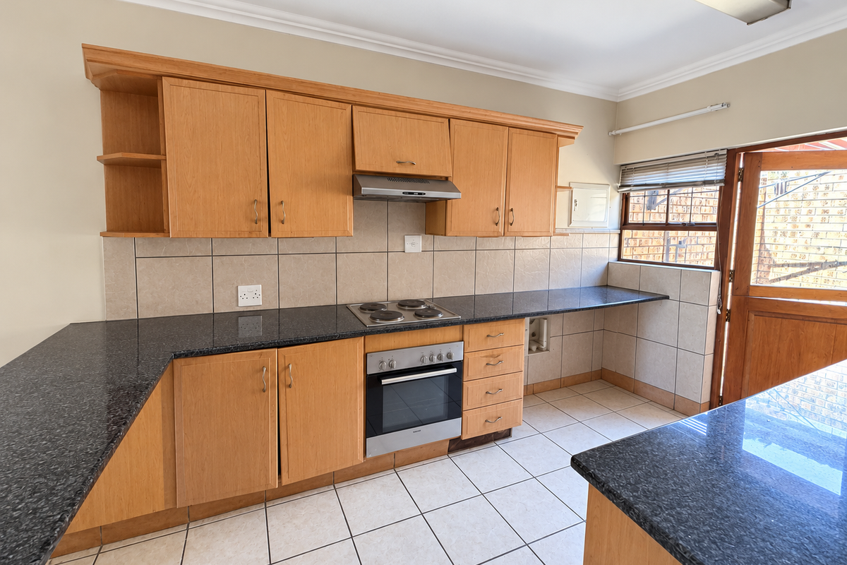 A functional kitchen featuring light wood cabinetry, dark granite countertops, built-in oven and hob, and direct access to the exterior.