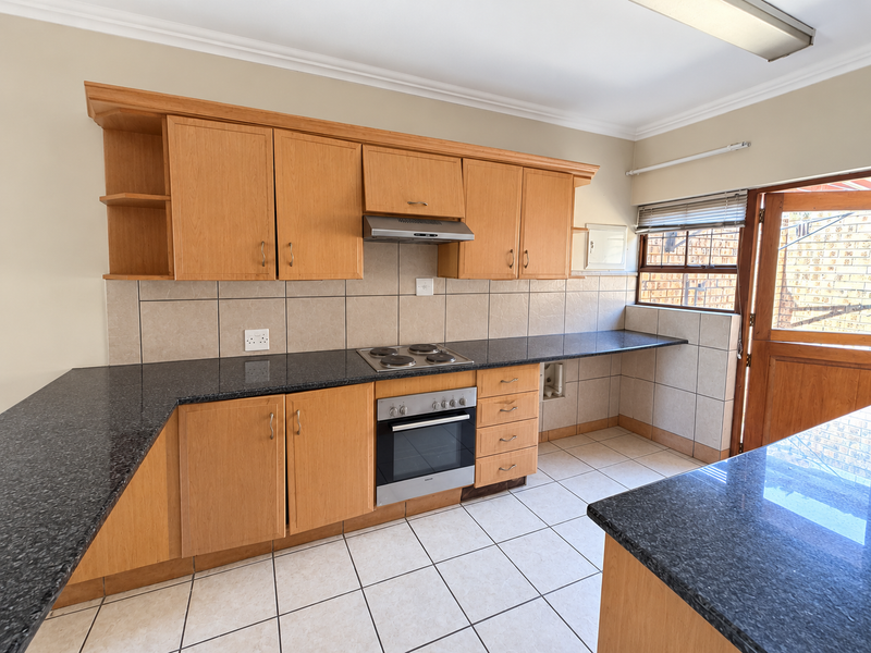 A functional kitchen featuring light wood cabinetry, dark granite countertops, built-in oven and hob, and direct access to the exterior.