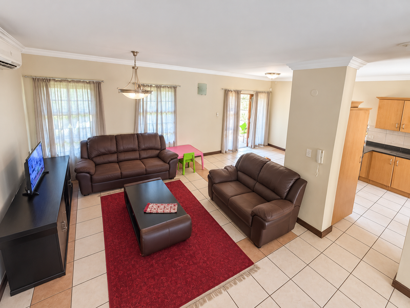 Spacious open-plan living area featuring tiled flooring, crown molding, and an integrated kitchen with wooden cabinetry, flowing out to a patio area.