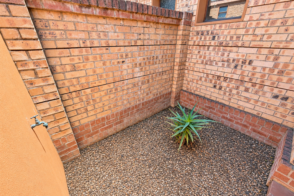 A private, low-maintenance rear courtyard area featuring brick boundary walls, gravel ground cover, and an external water tap.