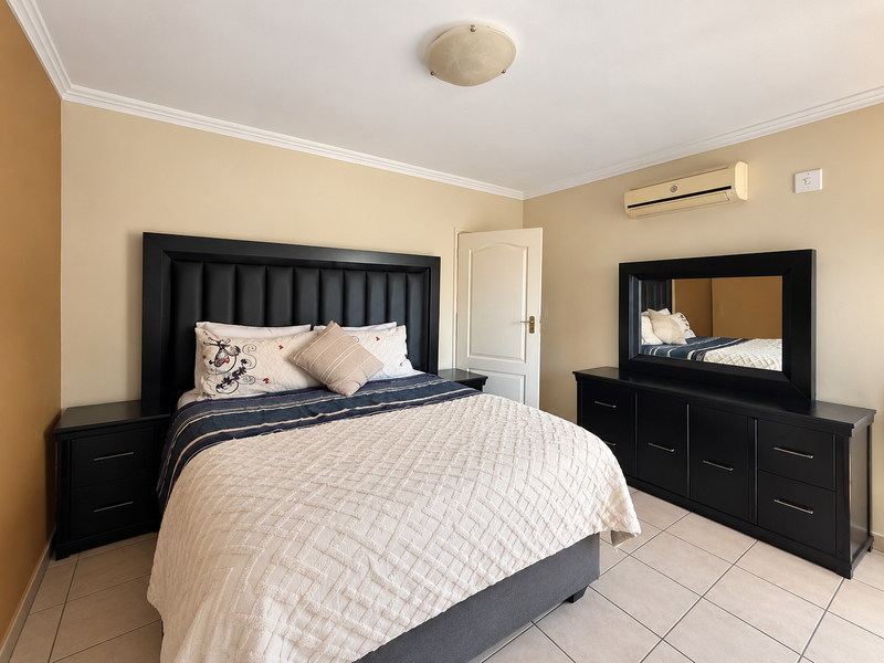 A well-maintained bedroom featuring tiled flooring, a wall-mounted air conditioning unit, and neutral wall tones.