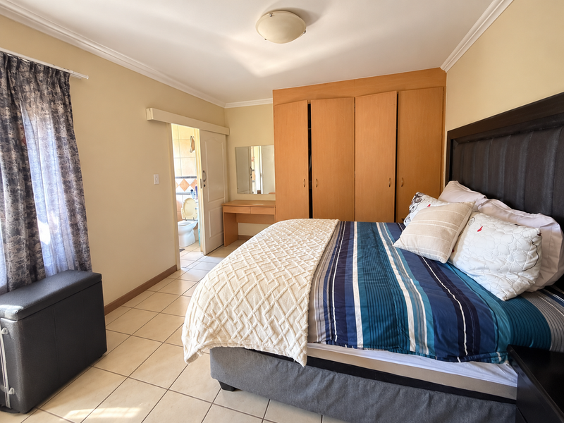 Spacious bedroom featuring built-in wooden cupboards, a vanity area, tiled flooring, and direct access to an en-suite bathroom.