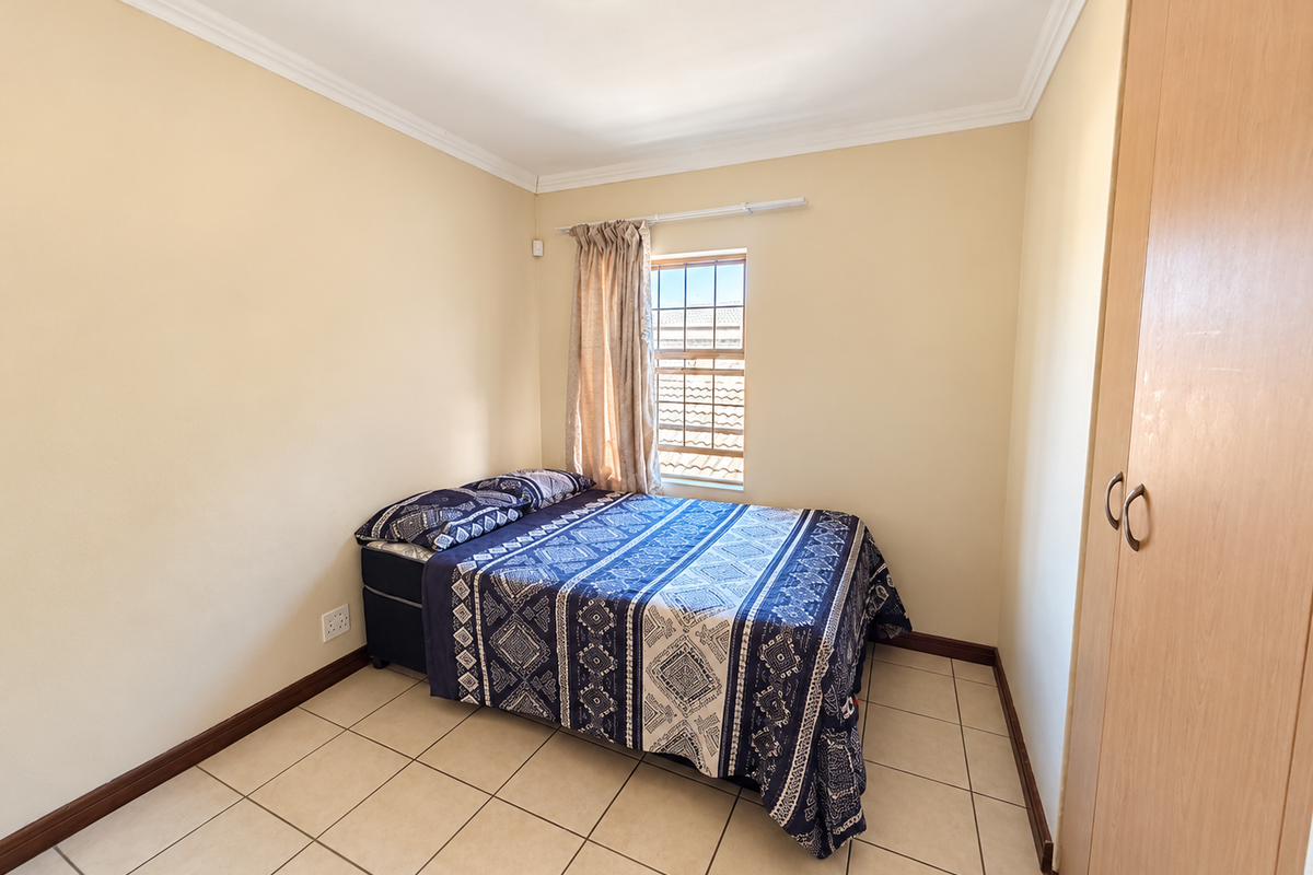 A functional bedroom featuring tiled flooring, a built-in wardrobe, and a window with security bars, providing a clean and practical living space.