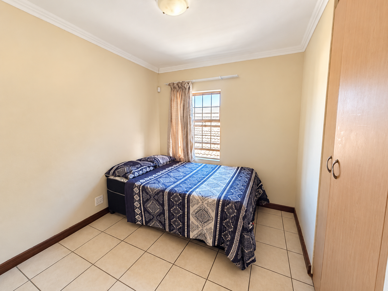 A functional bedroom featuring tiled flooring, a built-in wardrobe, and a window with security bars, providing a clean and practical living space.