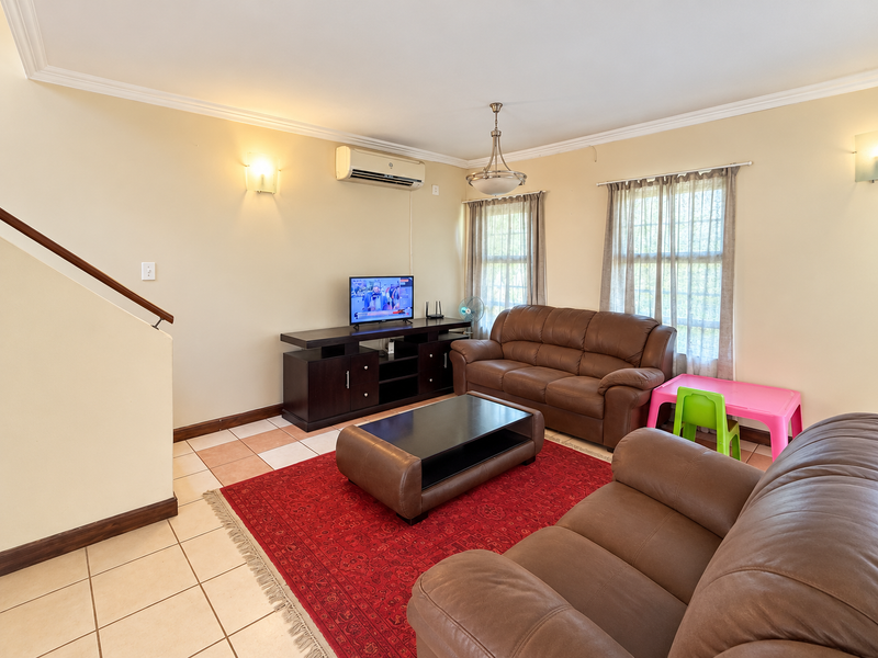 A comfortable living room featuring ceramic tile flooring, a split-system air conditioner, and a staircase with a wooden handrail.