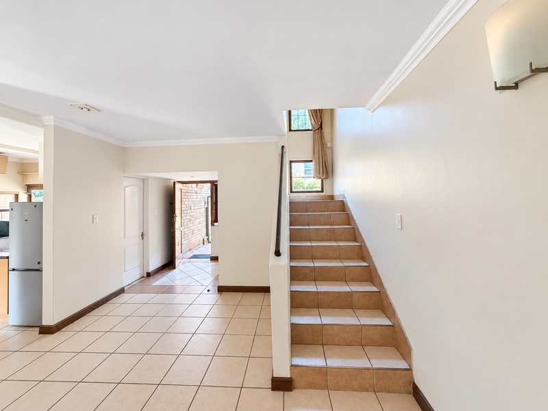 An open-plan entry area featuring tiled flooring, a staircase with a metal handrail, and neutral wall finishes leading towards the exterior entrance.